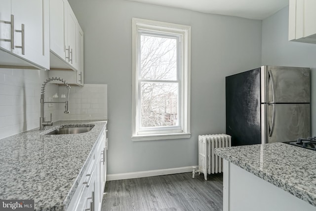 kitchen featuring radiator, white cabinets, dark hardwood / wood-style floors, light stone countertops, and stainless steel refrigerator