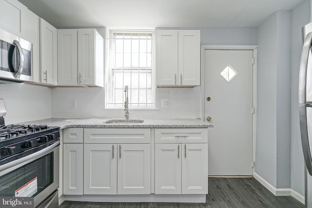 kitchen featuring appliances with stainless steel finishes, light stone counters, dark wood-type flooring, sink, and white cabinets