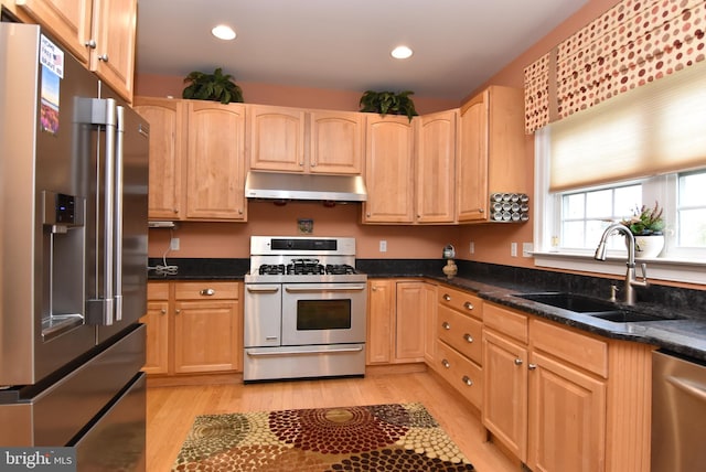 kitchen featuring light wood-type flooring, dark stone counters, stainless steel appliances, sink, and light brown cabinets