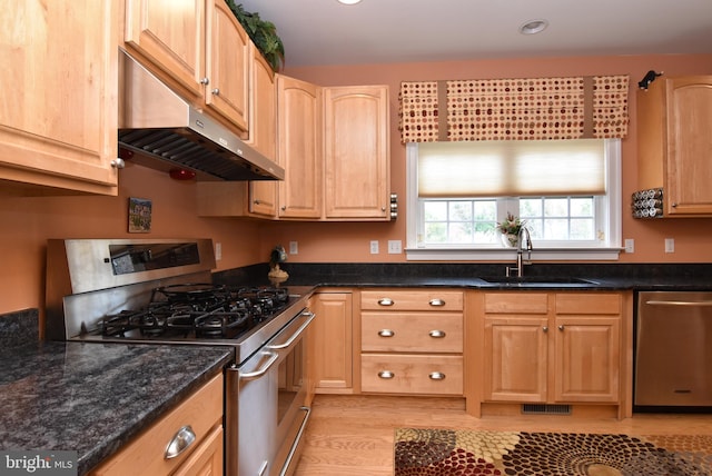 kitchen featuring light brown cabinetry, light wood-type flooring, dark stone counters, stainless steel appliances, and sink