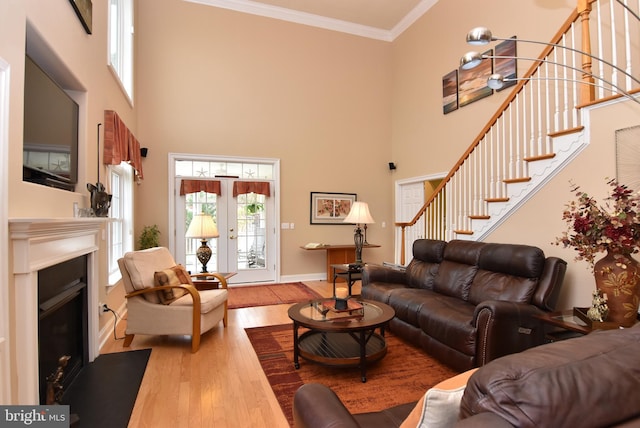 living room with crown molding, french doors, a towering ceiling, and light wood-type flooring