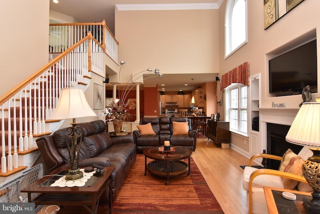 living room with light wood-type flooring, ornamental molding, and a towering ceiling