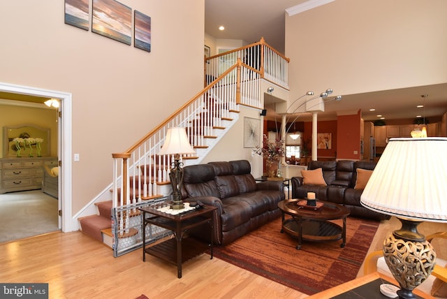 living room with light wood-type flooring, a towering ceiling, and crown molding