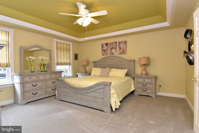 bedroom with a raised ceiling, ceiling fan, and light colored carpet