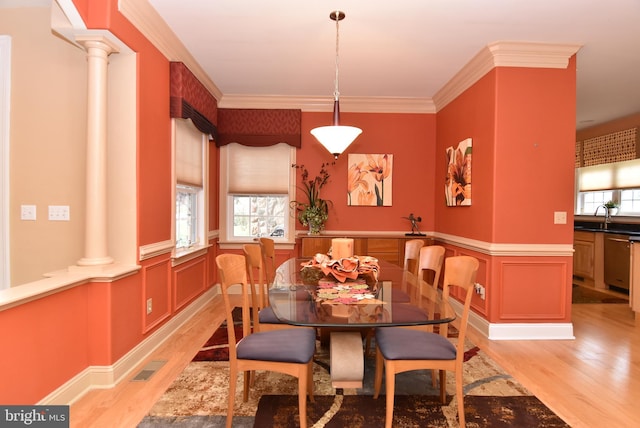 dining space featuring decorative columns, sink, ornamental molding, and light wood-type flooring