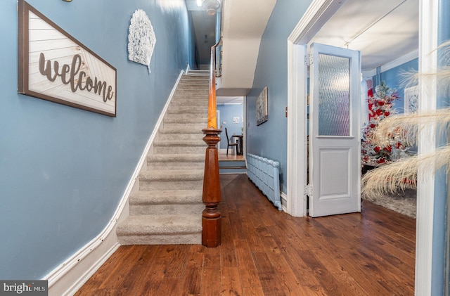 staircase featuring hardwood / wood-style flooring, radiator heating unit, and crown molding