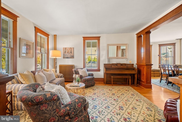 living room with decorative columns, light hardwood / wood-style flooring, radiator, and a healthy amount of sunlight