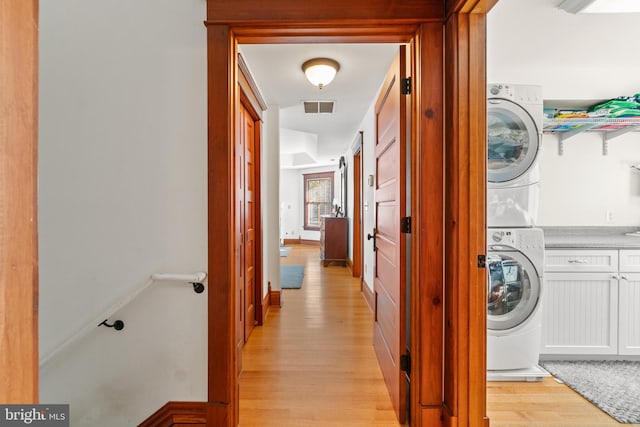 laundry area featuring cabinets, light wood-type flooring, and stacked washer / drying machine