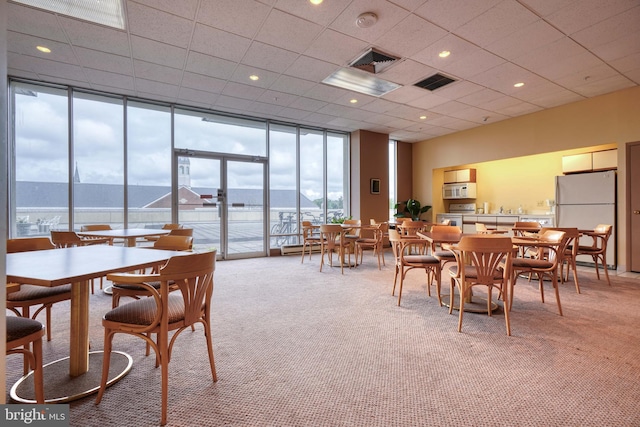 carpeted dining room featuring floor to ceiling windows, a drop ceiling, and a water view