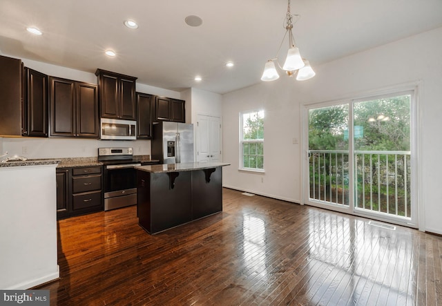 kitchen featuring appliances with stainless steel finishes, a kitchen island, a kitchen breakfast bar, hanging light fixtures, and plenty of natural light