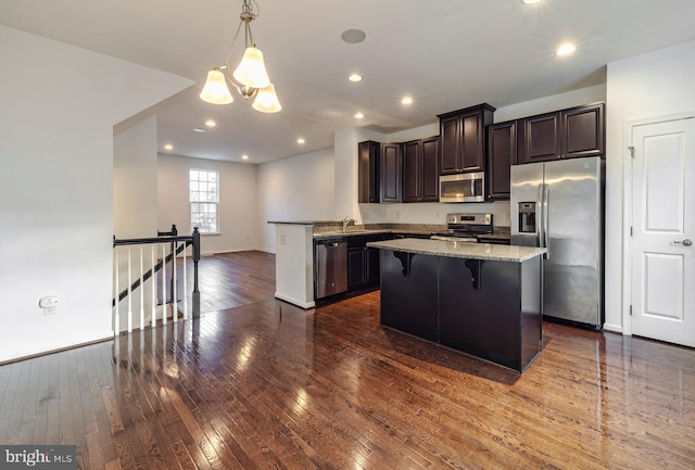 kitchen with a kitchen island, pendant lighting, light stone countertops, a kitchen breakfast bar, and stainless steel appliances