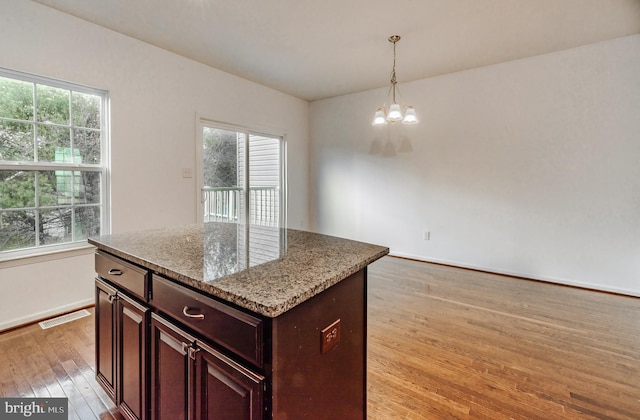 kitchen with light hardwood / wood-style floors, light stone countertops, a chandelier, pendant lighting, and a center island