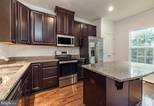 kitchen with dark brown cabinetry, appliances with stainless steel finishes, a center island, a breakfast bar, and light hardwood / wood-style flooring