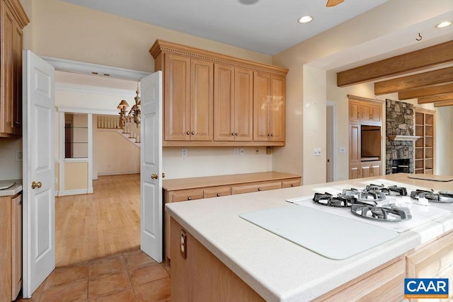 kitchen with light brown cabinets, light hardwood / wood-style flooring, a fireplace, beamed ceiling, and a kitchen island