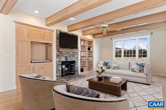 living room featuring ceiling fan, beam ceiling, a stone fireplace, and light hardwood / wood-style flooring