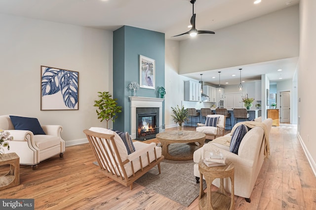 living room with ceiling fan, a towering ceiling, and light wood-type flooring