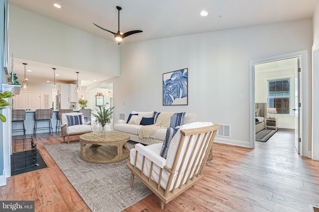 living room with ceiling fan, light wood-type flooring, and high vaulted ceiling