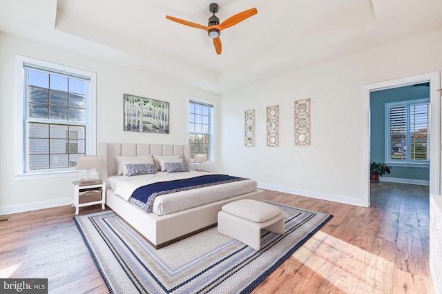 bedroom featuring ceiling fan, a tray ceiling, and light hardwood / wood-style flooring