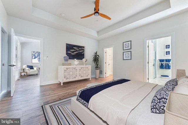 bedroom featuring wood-type flooring, ensuite bathroom, ceiling fan, and a tray ceiling