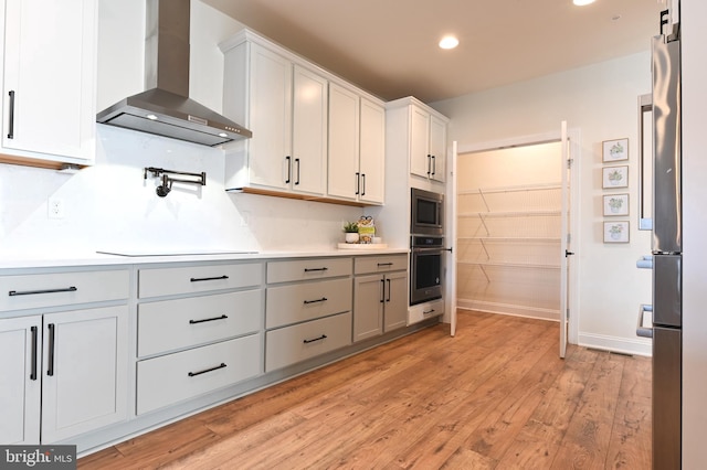 kitchen with white cabinets, light wood-type flooring, wall chimney range hood, and stainless steel appliances