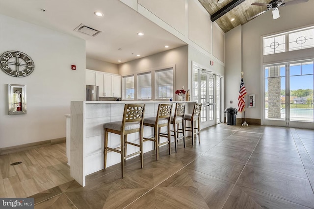 kitchen featuring a kitchen bar, stainless steel fridge, ceiling fan, high vaulted ceiling, and white cabinets