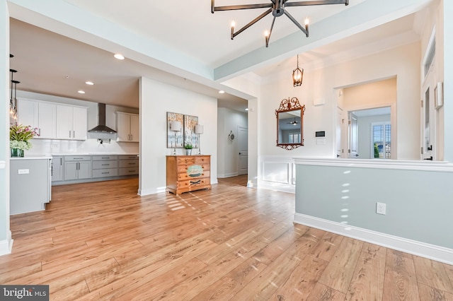 kitchen featuring an inviting chandelier, wall chimney range hood, light hardwood / wood-style flooring, decorative light fixtures, and white cabinetry