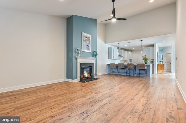 living room with ceiling fan, light hardwood / wood-style flooring, and a towering ceiling