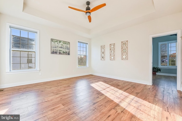 spare room with ceiling fan, light wood-type flooring, and a tray ceiling