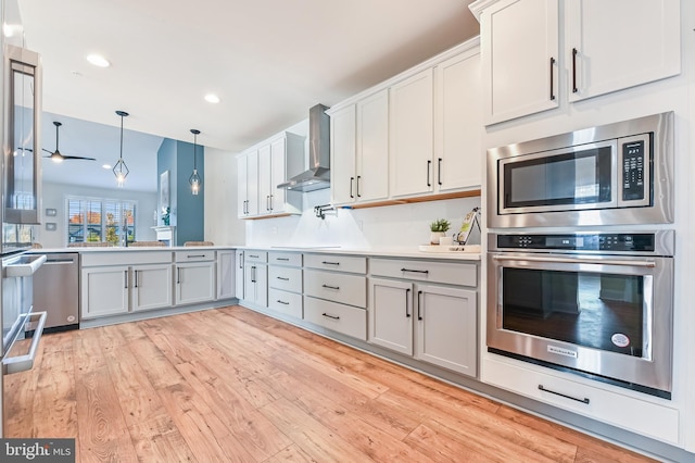 kitchen with stainless steel appliances, light hardwood / wood-style flooring, hanging light fixtures, and wall chimney exhaust hood