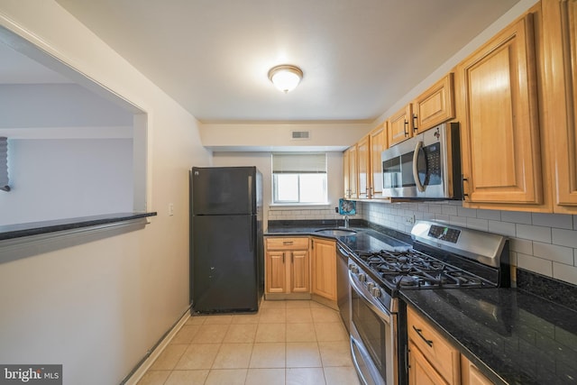 kitchen featuring dark stone counters, sink, decorative backsplash, light tile patterned floors, and stainless steel appliances