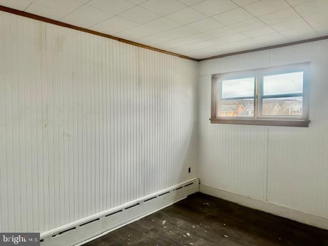 empty room with crown molding, dark wood-type flooring, and a baseboard heating unit