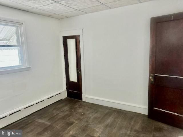 empty room with a paneled ceiling, dark wood-type flooring, and a baseboard radiator