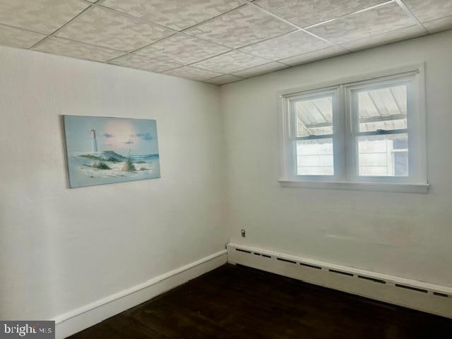 empty room featuring wood-type flooring, a paneled ceiling, and baseboard heating