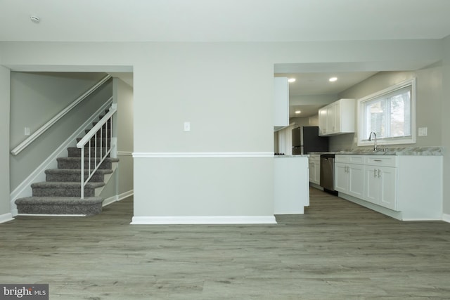 kitchen with sink, black fridge, stainless steel dishwasher, light hardwood / wood-style floors, and white cabinets