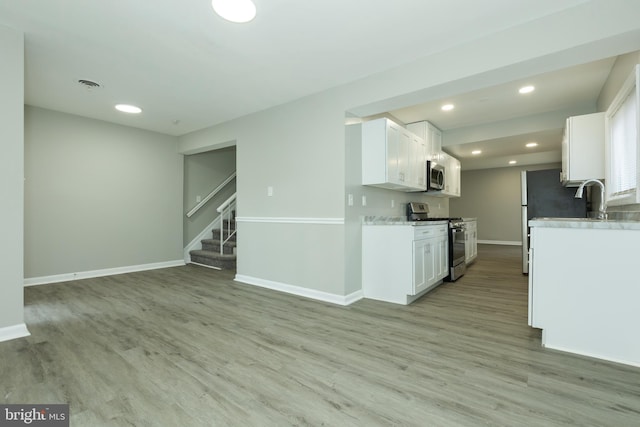 kitchen featuring light wood-type flooring, white cabinetry, light stone counters, and appliances with stainless steel finishes