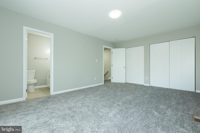 unfurnished bedroom with ensuite bathroom, light carpet, and multiple closets