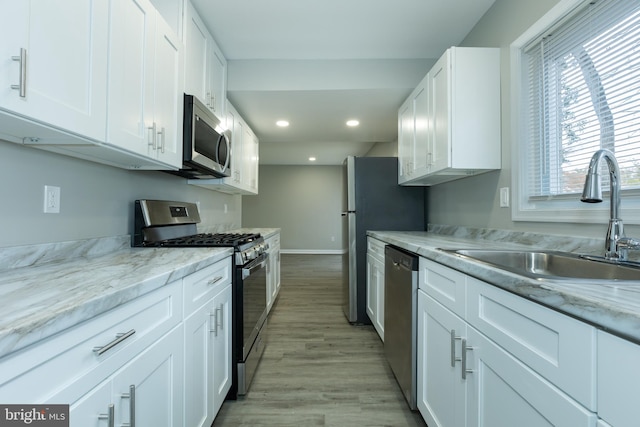 kitchen with white cabinets, sink, light wood-type flooring, appliances with stainless steel finishes, and light stone counters