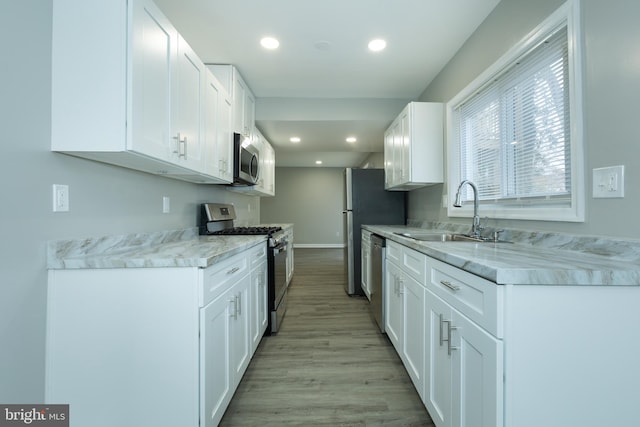 kitchen with light stone countertops, light wood-type flooring, stainless steel appliances, sink, and white cabinetry