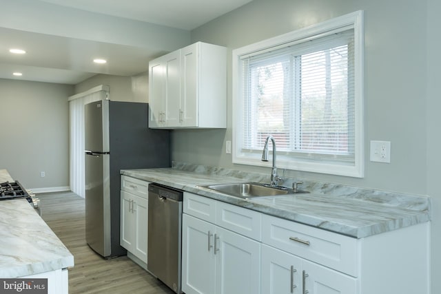 kitchen with appliances with stainless steel finishes, light stone counters, sink, light hardwood / wood-style flooring, and white cabinets