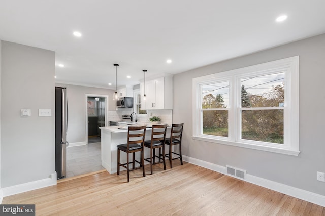 kitchen featuring kitchen peninsula, appliances with stainless steel finishes, a breakfast bar, light hardwood / wood-style flooring, and white cabinets