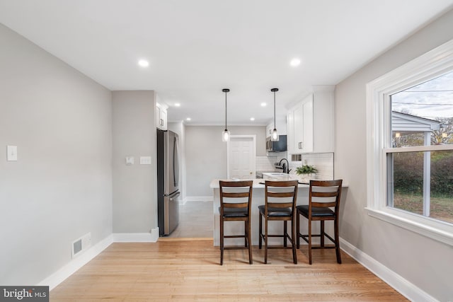 kitchen with stainless steel appliances, backsplash, kitchen peninsula, white cabinets, and light wood-type flooring