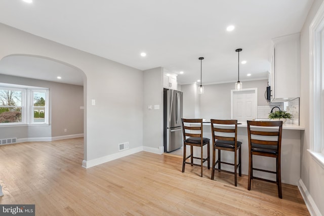 kitchen with white cabinets, decorative backsplash, decorative light fixtures, light hardwood / wood-style floors, and stainless steel refrigerator