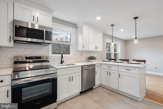 kitchen featuring white cabinetry, sink, hanging light fixtures, kitchen peninsula, and appliances with stainless steel finishes