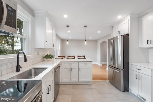 kitchen with appliances with stainless steel finishes, backsplash, sink, white cabinets, and hanging light fixtures