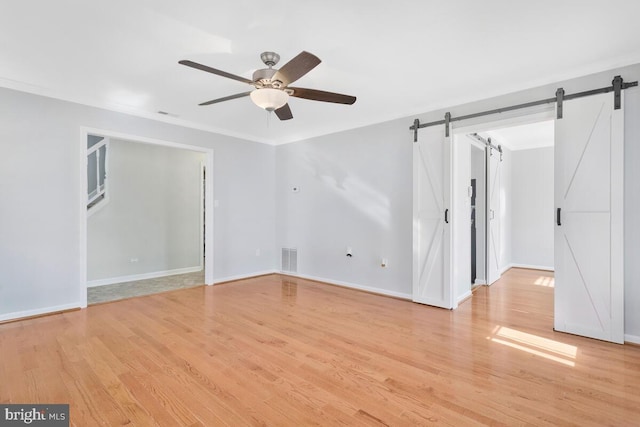 empty room featuring crown molding, light hardwood / wood-style flooring, a barn door, and ceiling fan