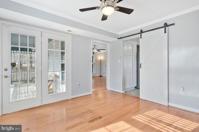 spare room featuring light hardwood / wood-style floors, ornamental molding, a barn door, and ceiling fan