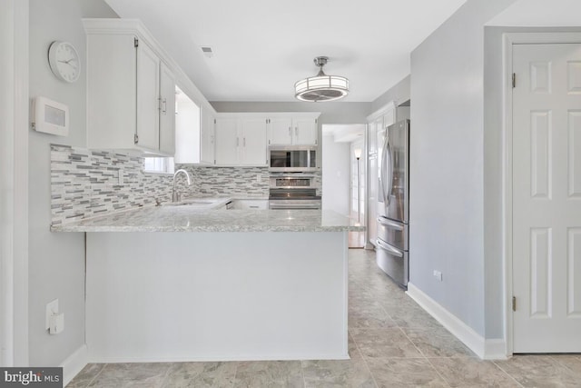 kitchen featuring white cabinetry, stainless steel appliances, kitchen peninsula, and light stone counters