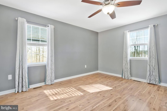 empty room with a wealth of natural light, ceiling fan, and light hardwood / wood-style flooring