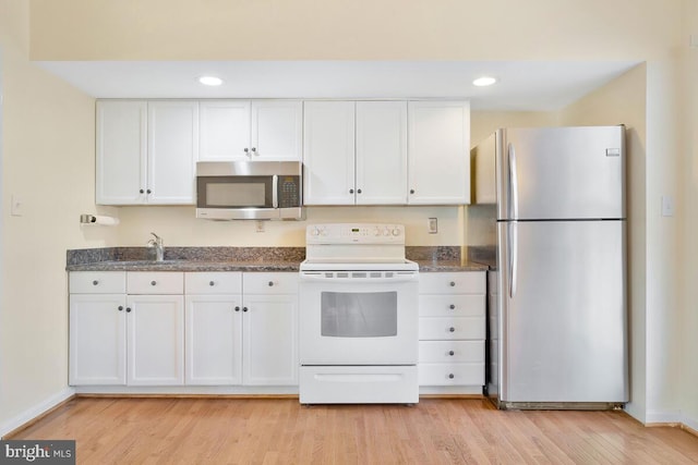 kitchen with white cabinetry, appliances with stainless steel finishes, light hardwood / wood-style flooring, and dark stone counters