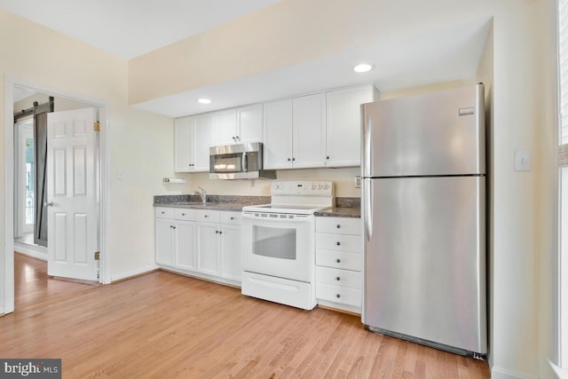 kitchen with light wood-type flooring, a barn door, white cabinets, and appliances with stainless steel finishes